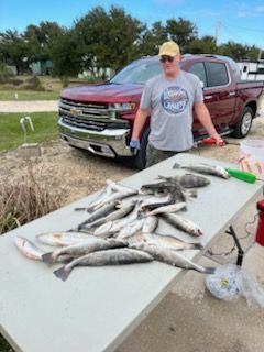 Man stands by a table with many fish, a red truck in the background, likely after fishing.