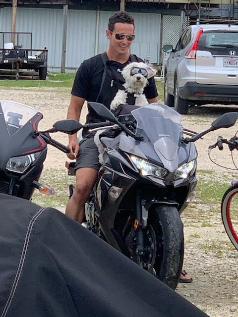 Man on motorcycle with dog in carrier wearing sunglasses. Outdoors.