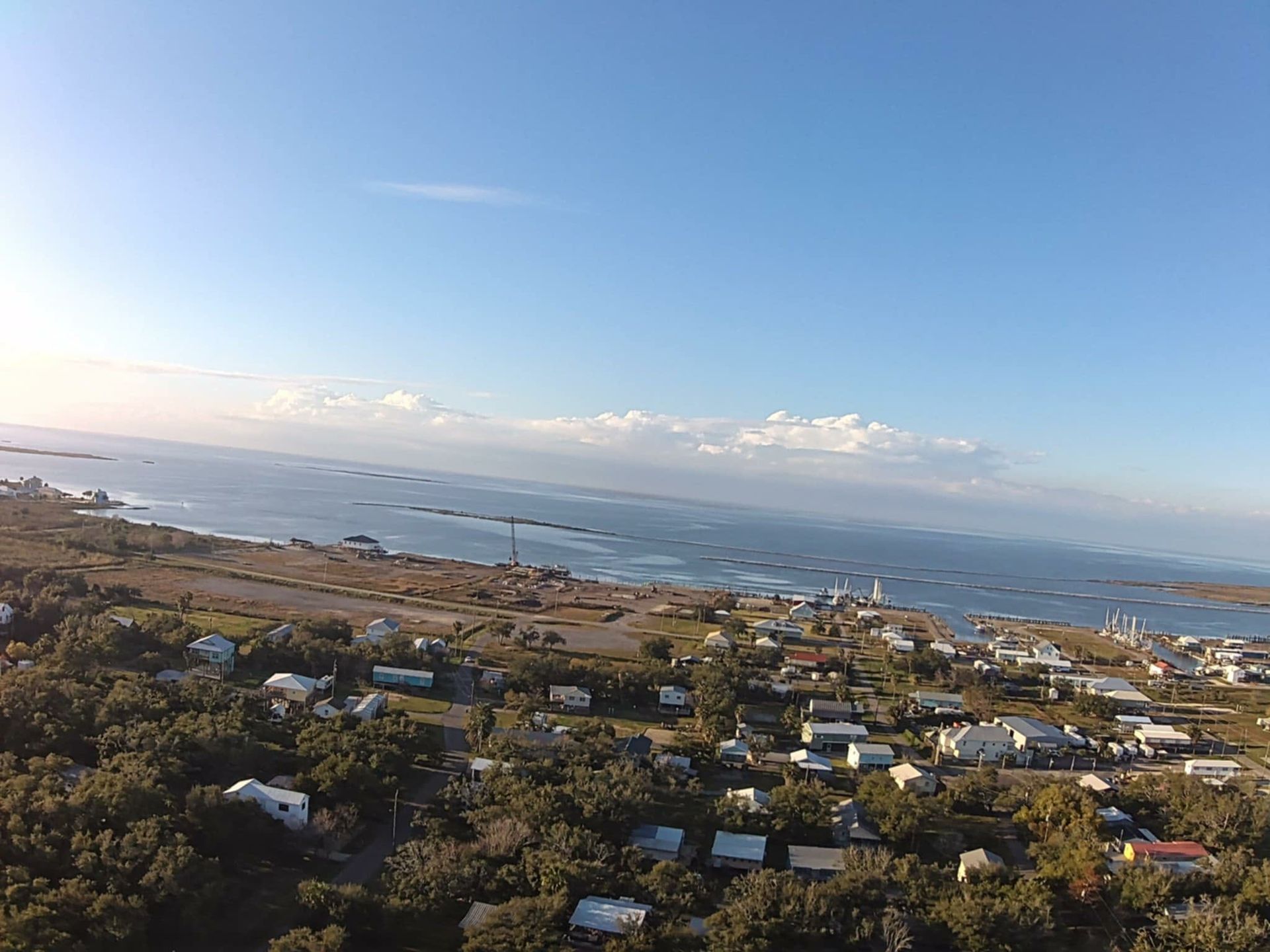 Aerial view of a coastal town with buildings and trees near the ocean under a clear, blue sky.
