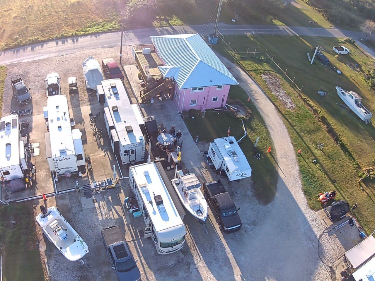Aerial view of a pink building with a turquoise roof, surrounded by RVs, boats, and trucks parked on a gravel lot.