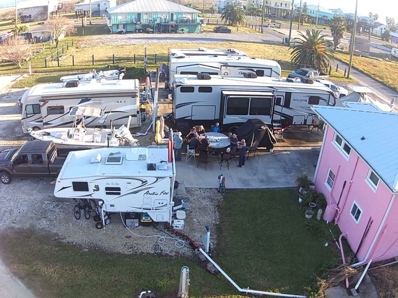 Campground with RVs, a gazebo, and a pink building. People are gathered at a table.