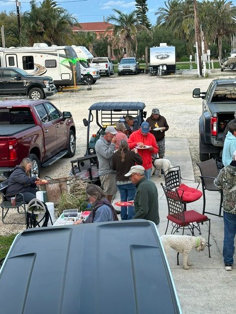 People gather near RVs and trucks, eating outdoors.