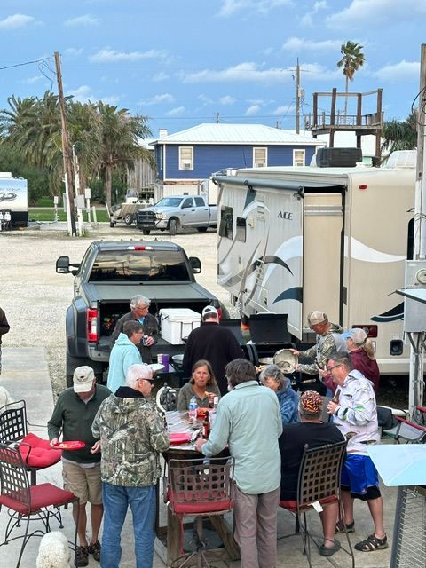 Group of people gathered around tables, likely eating, near RVs and a truck outdoors.