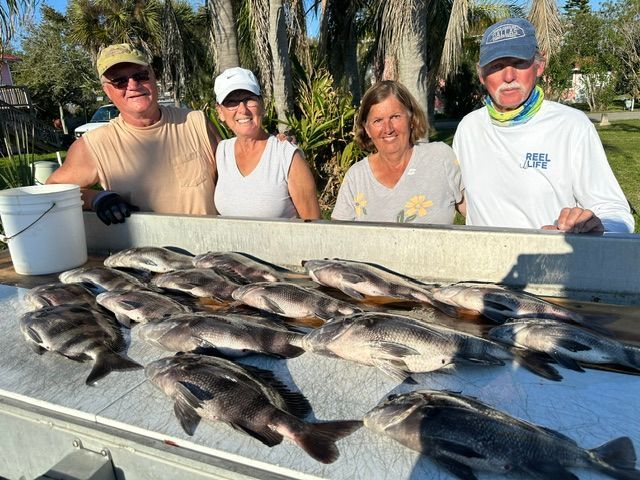 Four people pose behind a table covered in freshly caught fish; sunny outdoor setting.