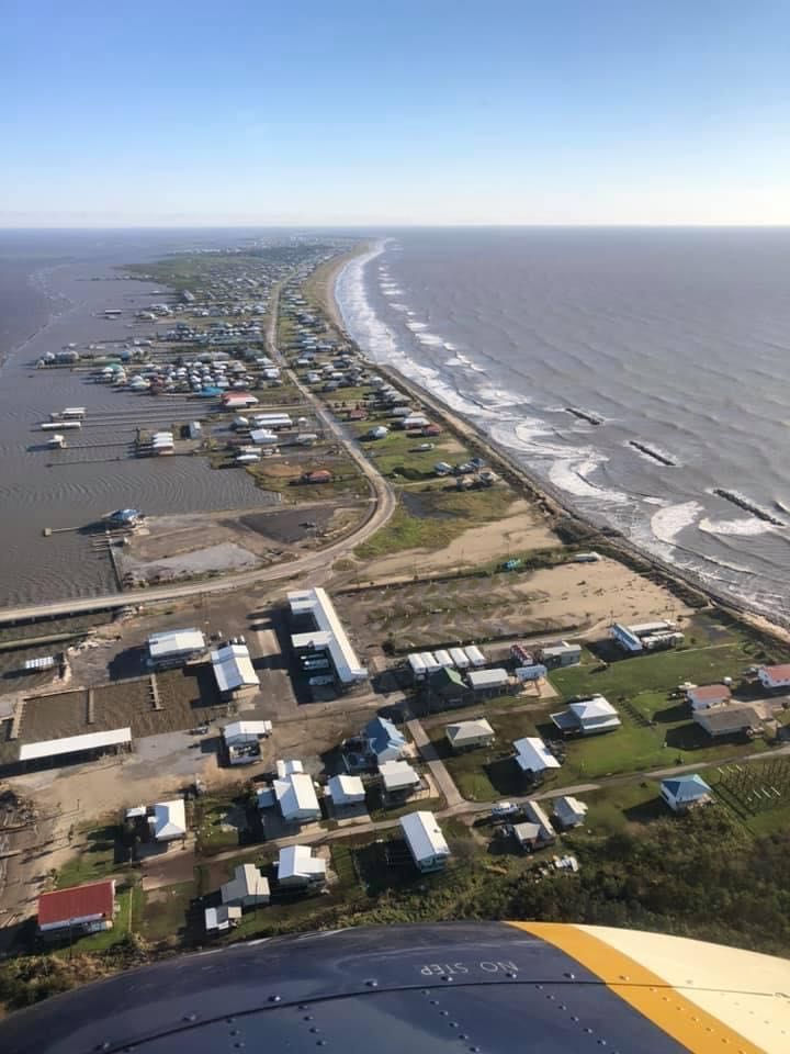 Aerial view of a coastal town, houses lining a narrow strip of land between water and the ocean.