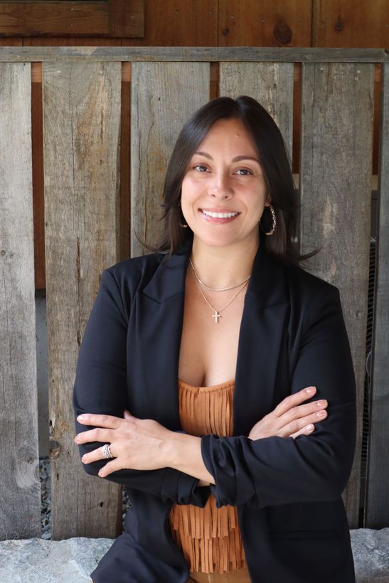 A woman is sitting at a desk with a laptop and a vase of flowers.