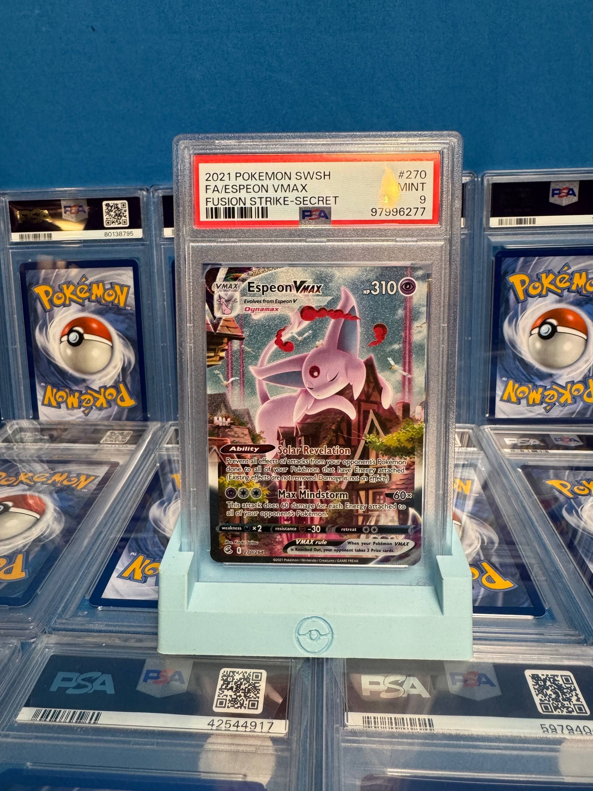 A graded Espeon VMAX Pokemon card in a blue holder, surrounded by other graded cards.