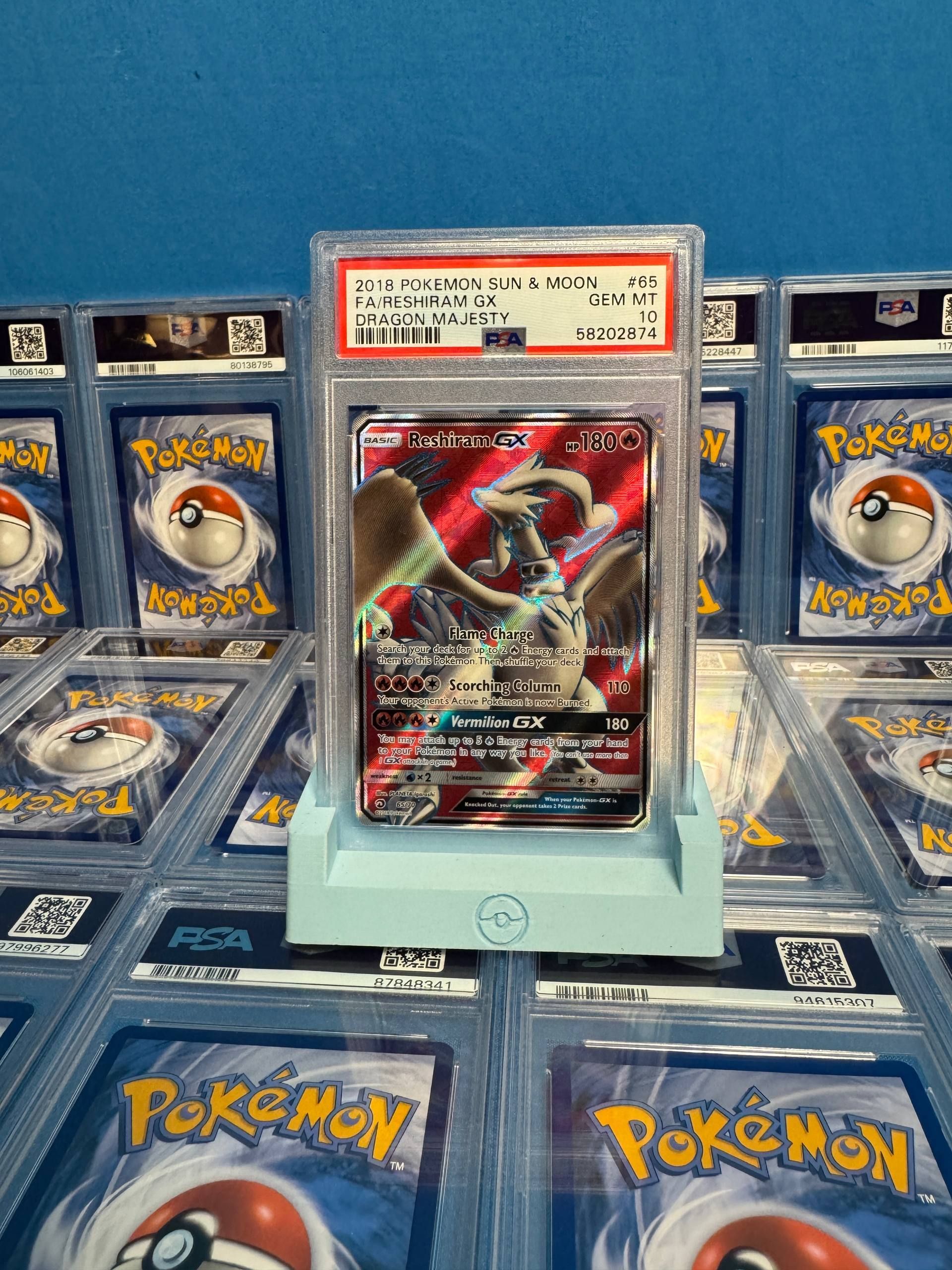 A graded Reshiram & Charizard card on a stand, surrounded by other Pokémon cards in cases.