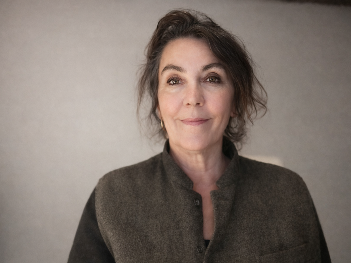 Woman with dark hair, smiling, wearing a dark gray jacket against a light background.