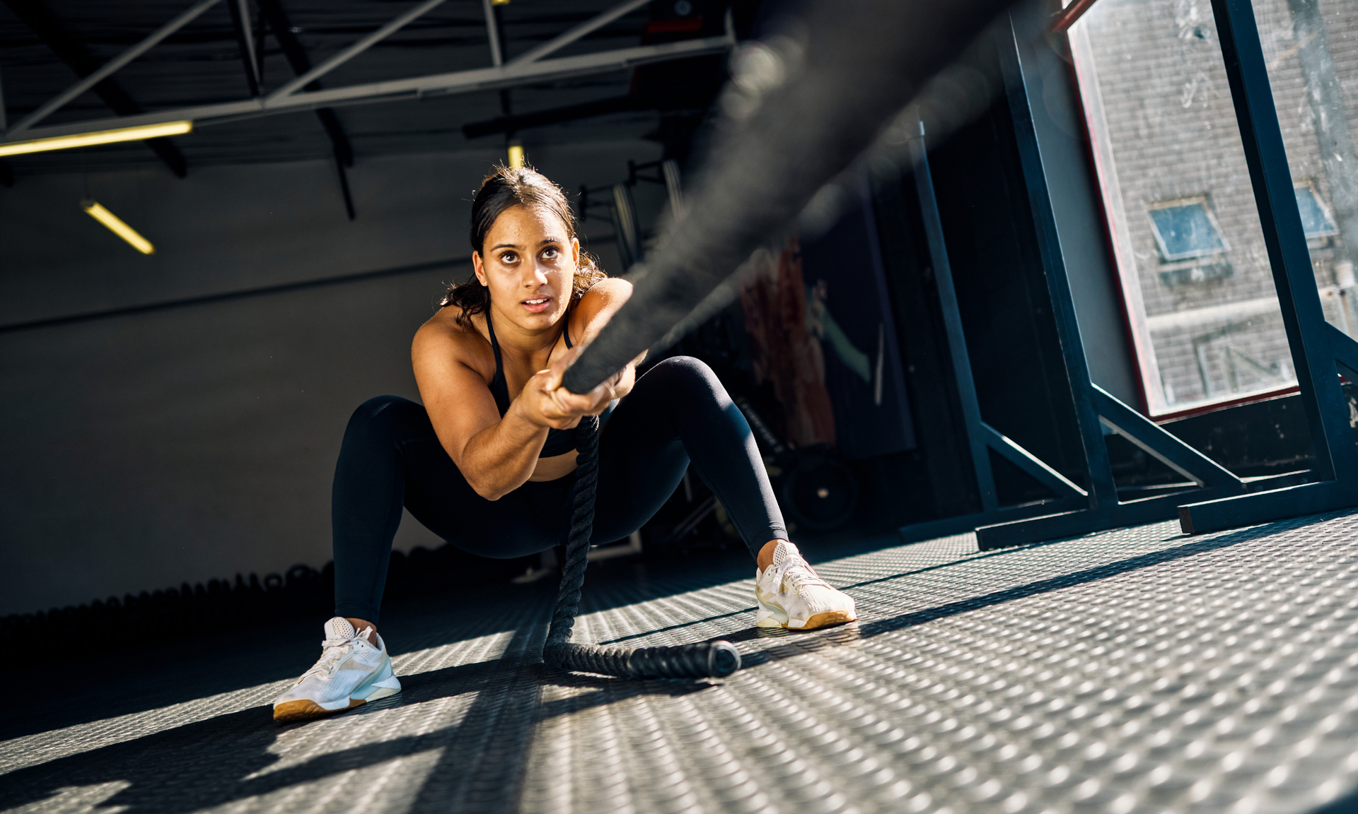 Vrouw in sportkleding trekt aan een dik touw, geconcentreerde uitdrukking, in de sportschool.