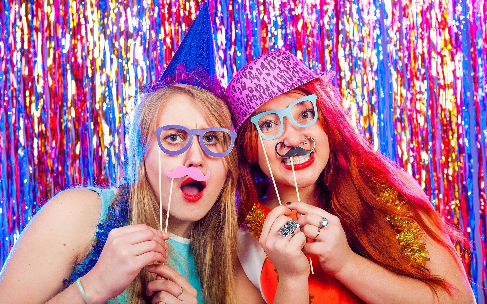 Two girls are posing for a picture in a photo booth with party props.