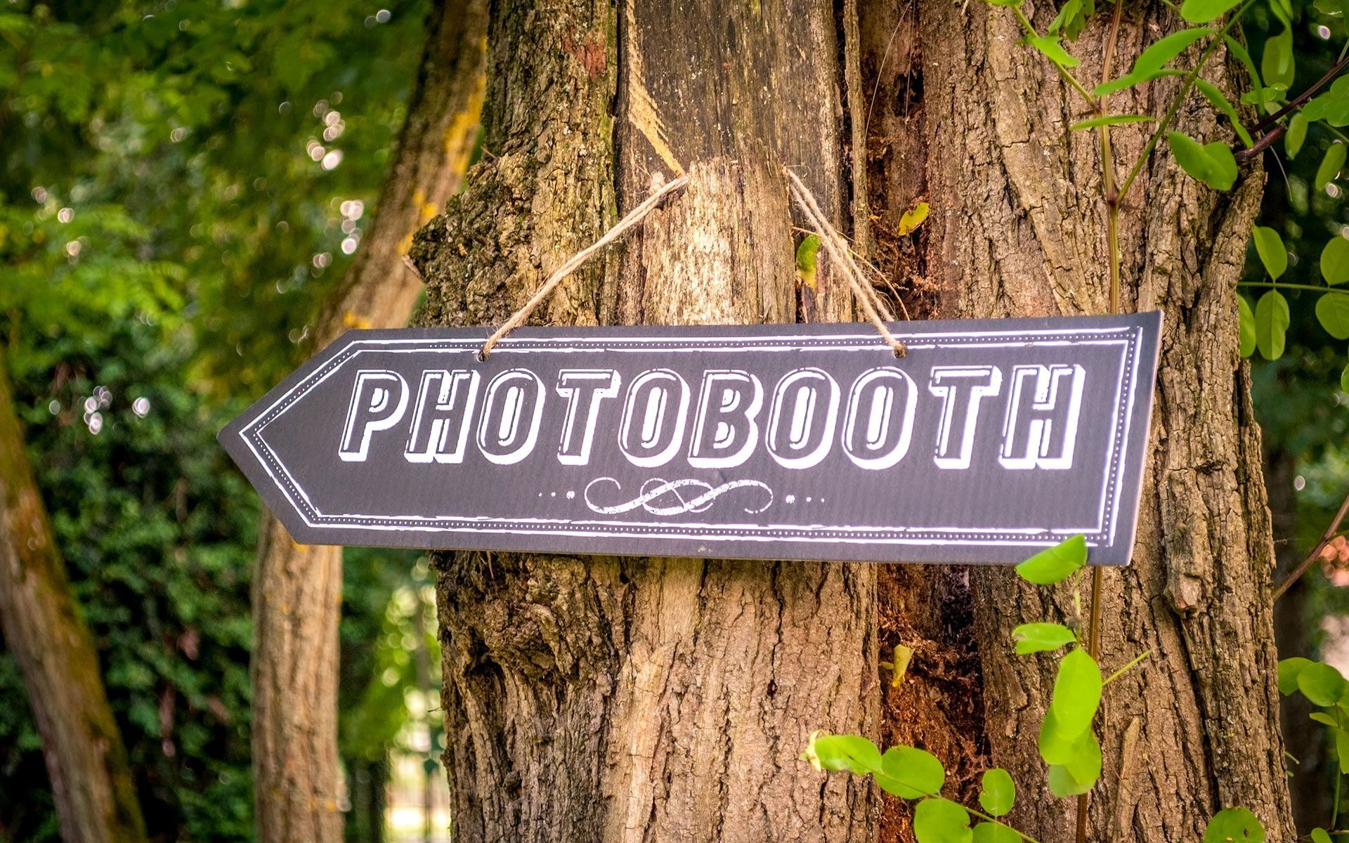A sign that says photobooth is hanging on a tree.