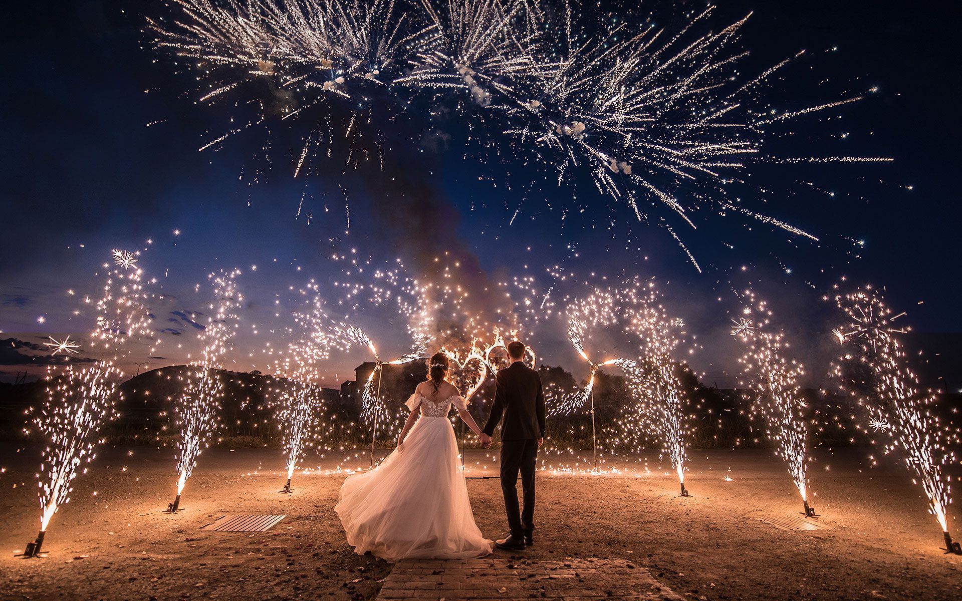 A bride and groom are standing in front of a fireworks display.