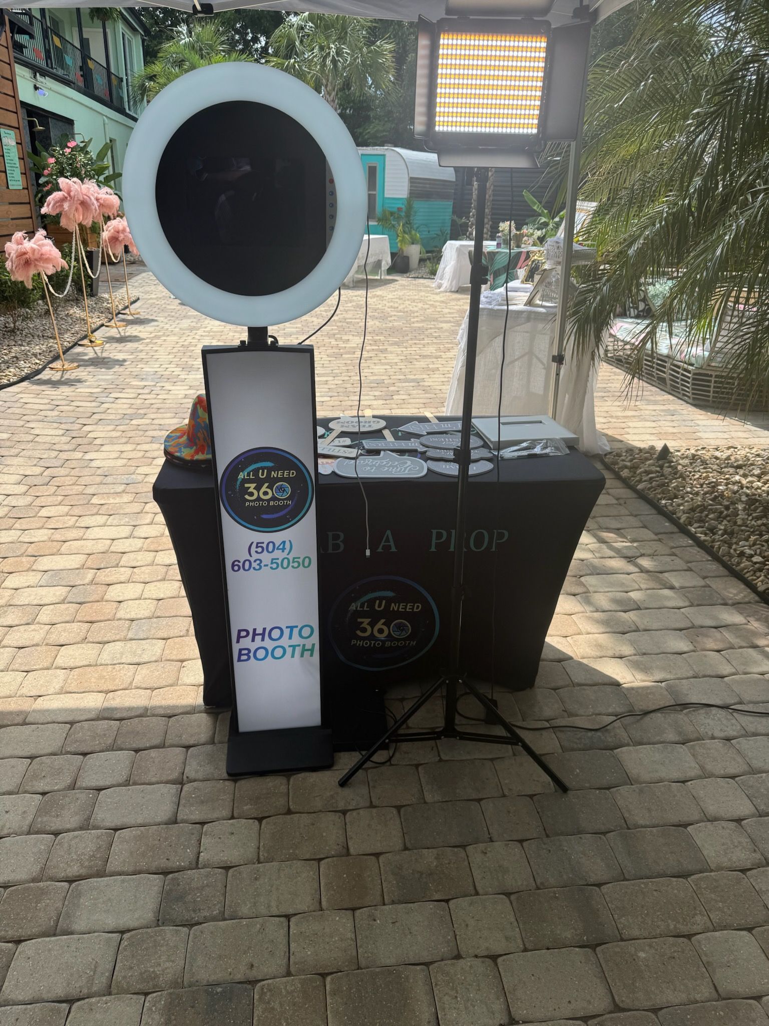 A 360 photo booth set up outdoors on a patio. It has a ring light and props on a black table.
