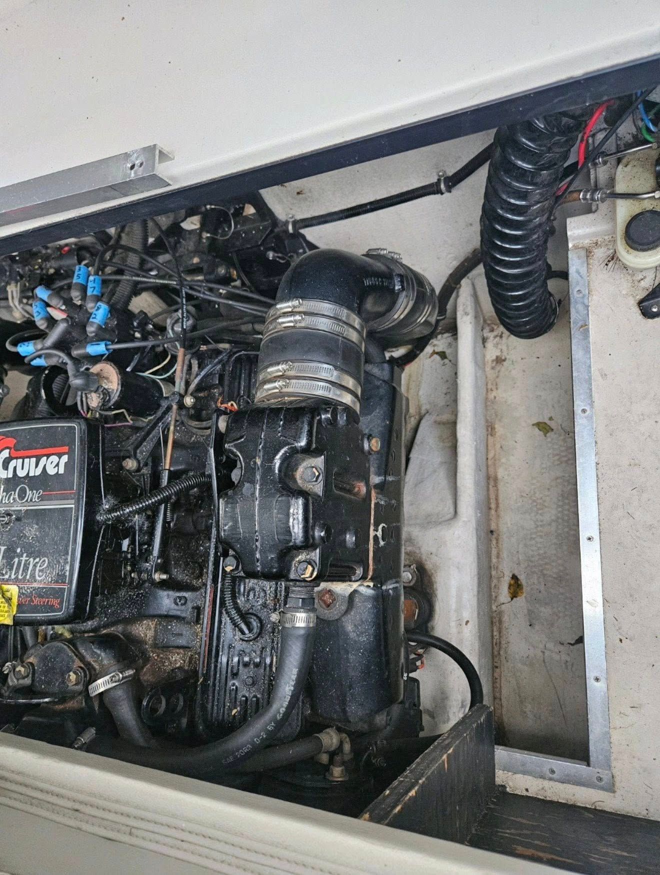 Boat engine, black, with attached hoses and wires, in a white compartment.