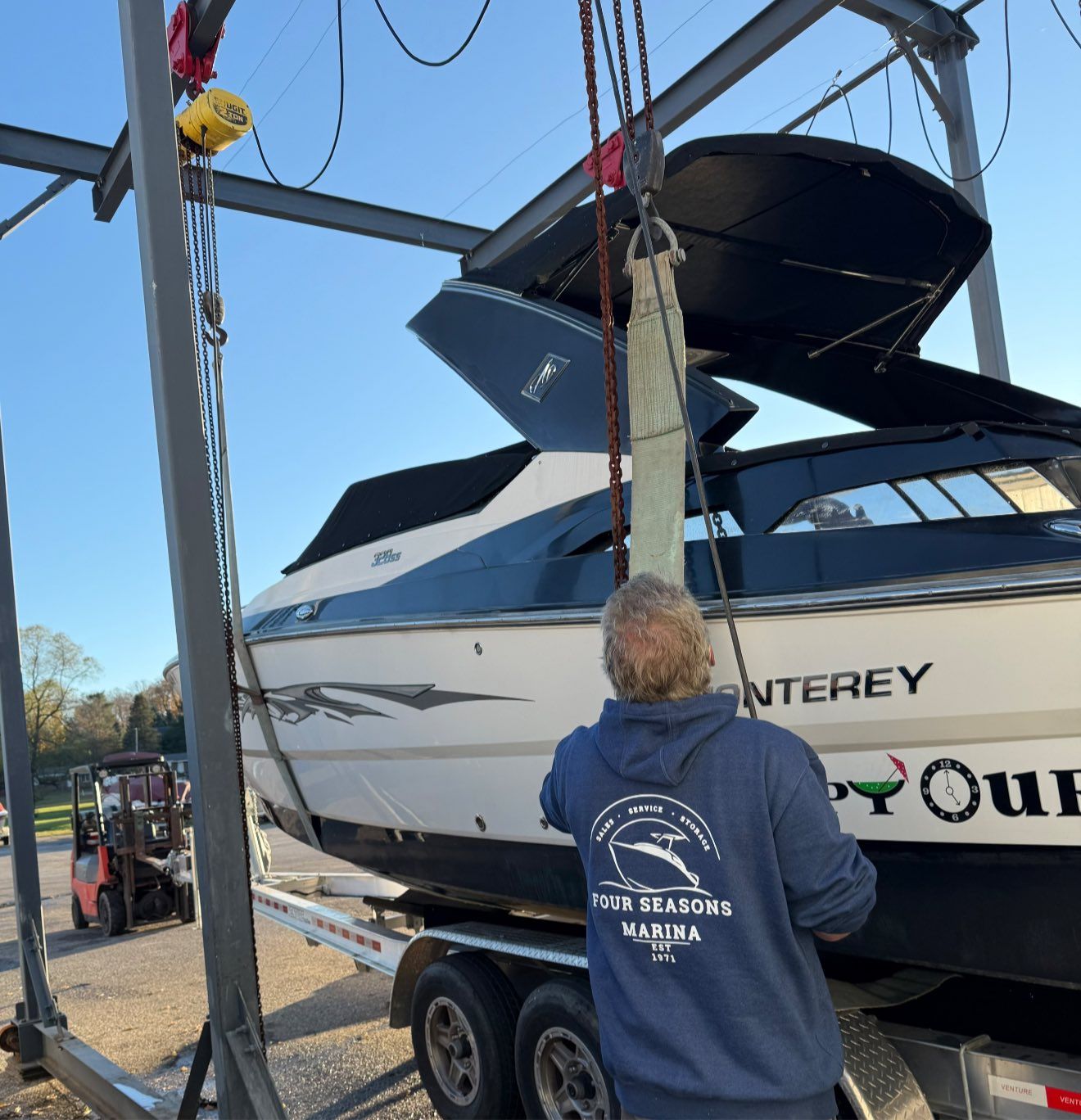 A person guiding a boat being lifted by a crane at a marina.