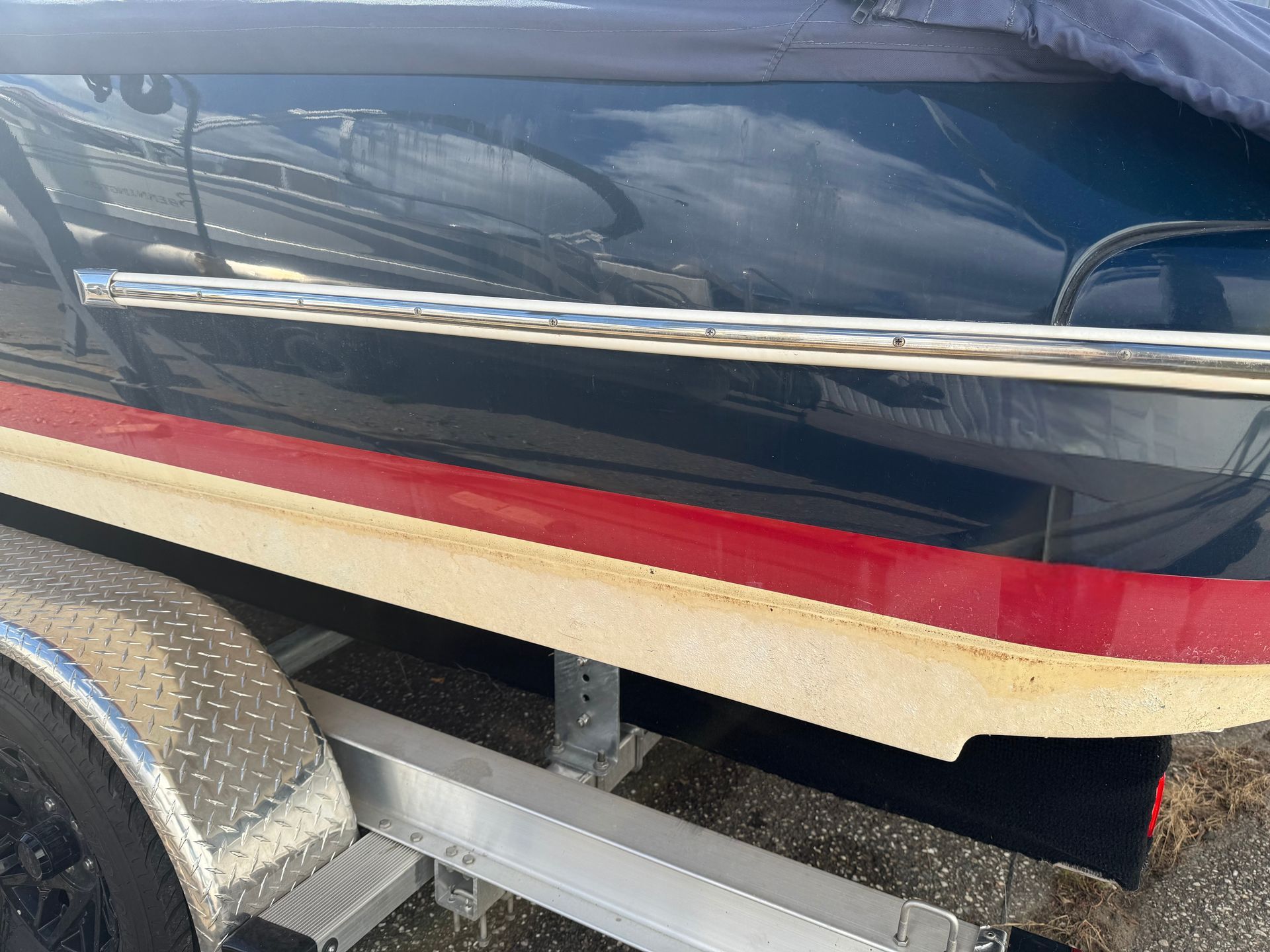 Boat on trailer, blue hull with red stripe, stainless steel rail, and off-white hull bottom.