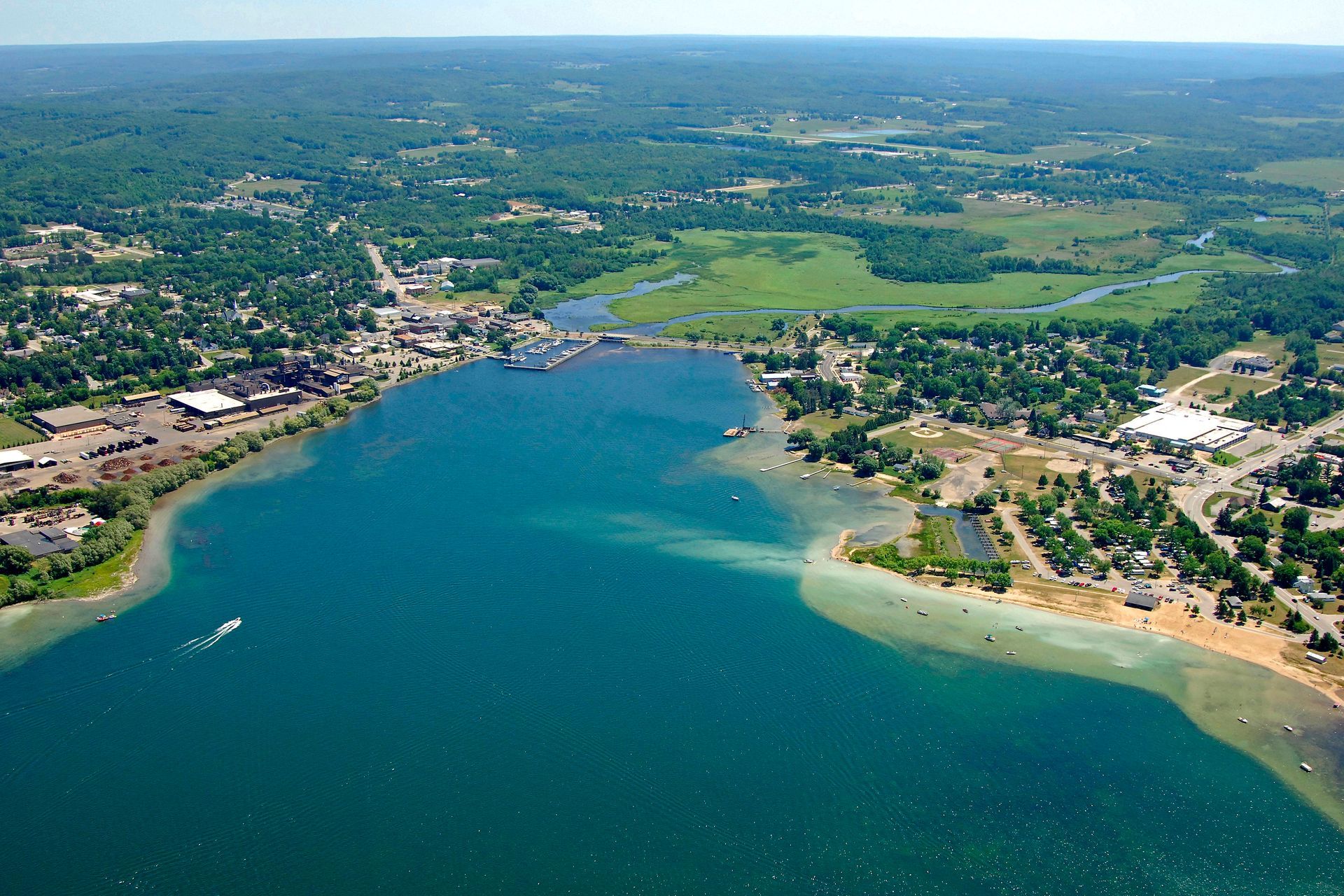 Aerial view of a town on a blue lake, with green trees, buildings, and a bridge.