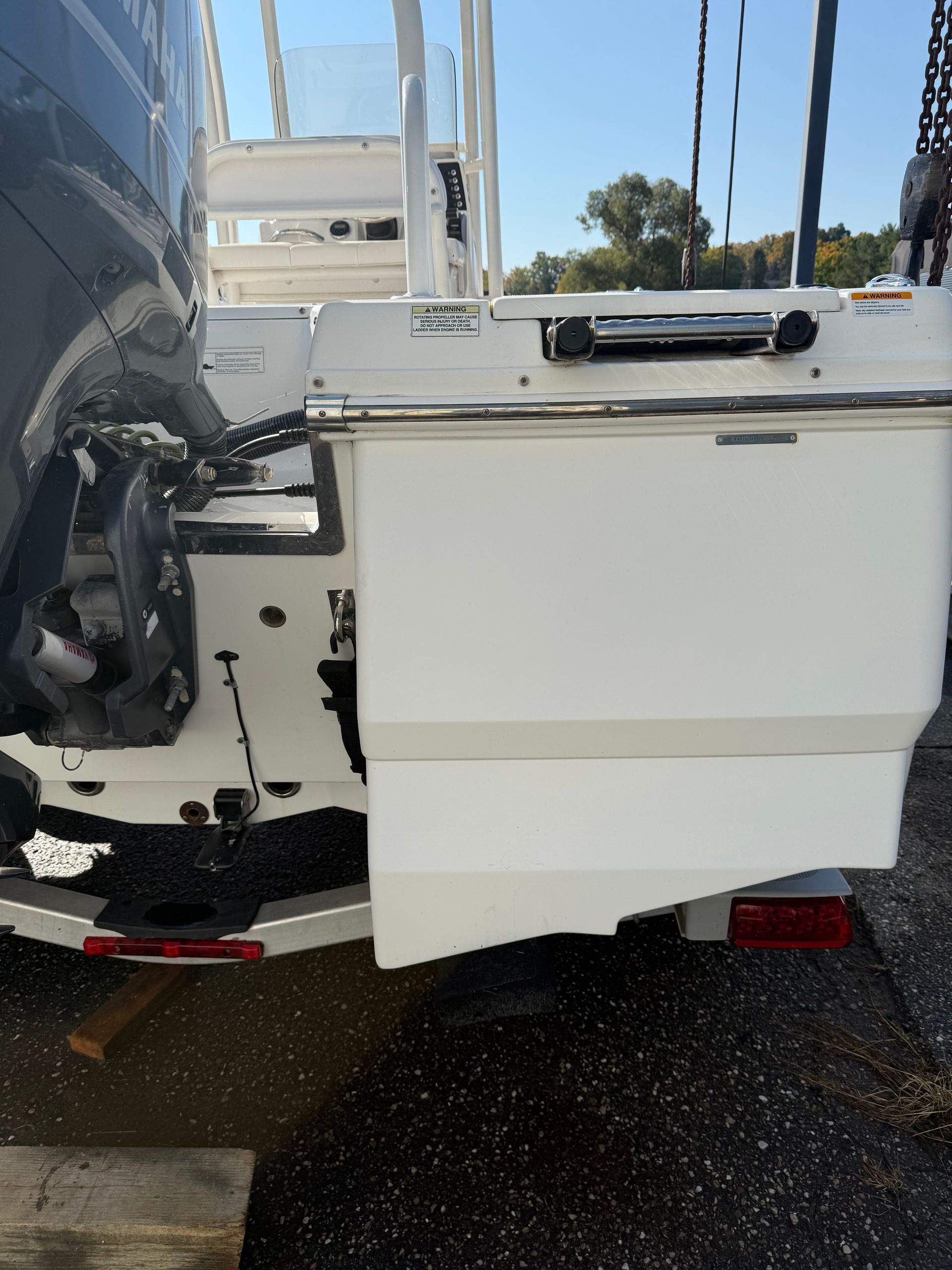 Back of a white motorboat with an outboard motor, docked on pavement.