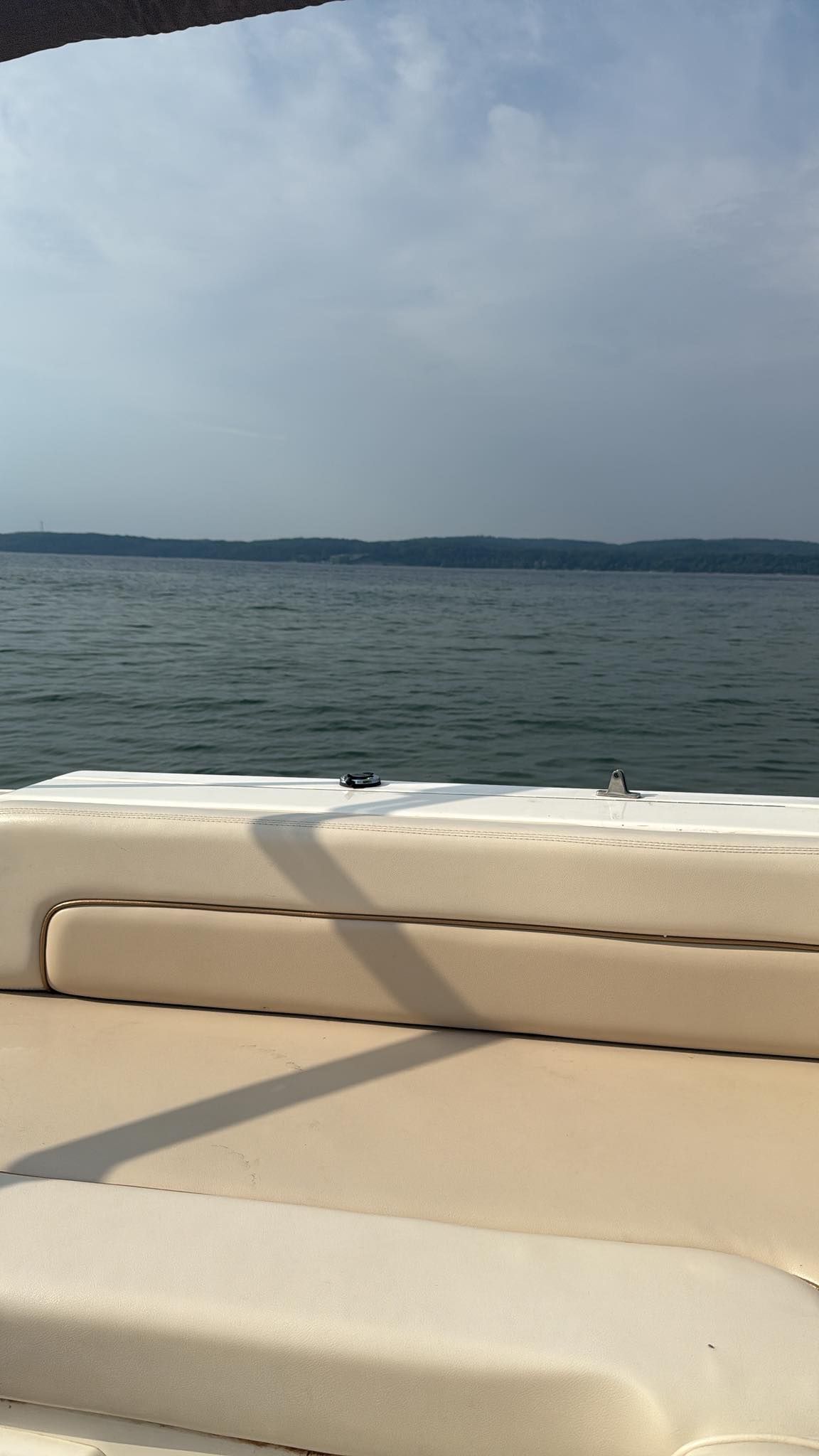 Boat interior with a view of a lake and distant shoreline under a cloudy sky.