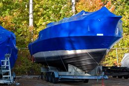 Blue-covered boat on trailer, outdoors. Surrounded by trees.