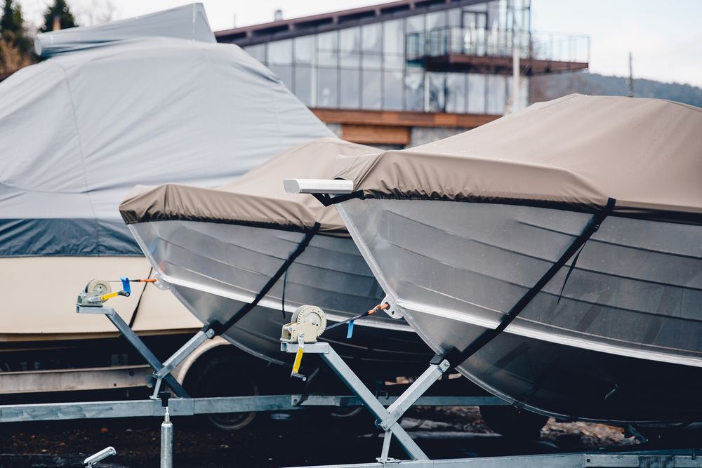 Boats covered with tan and gray tarps on trailers.