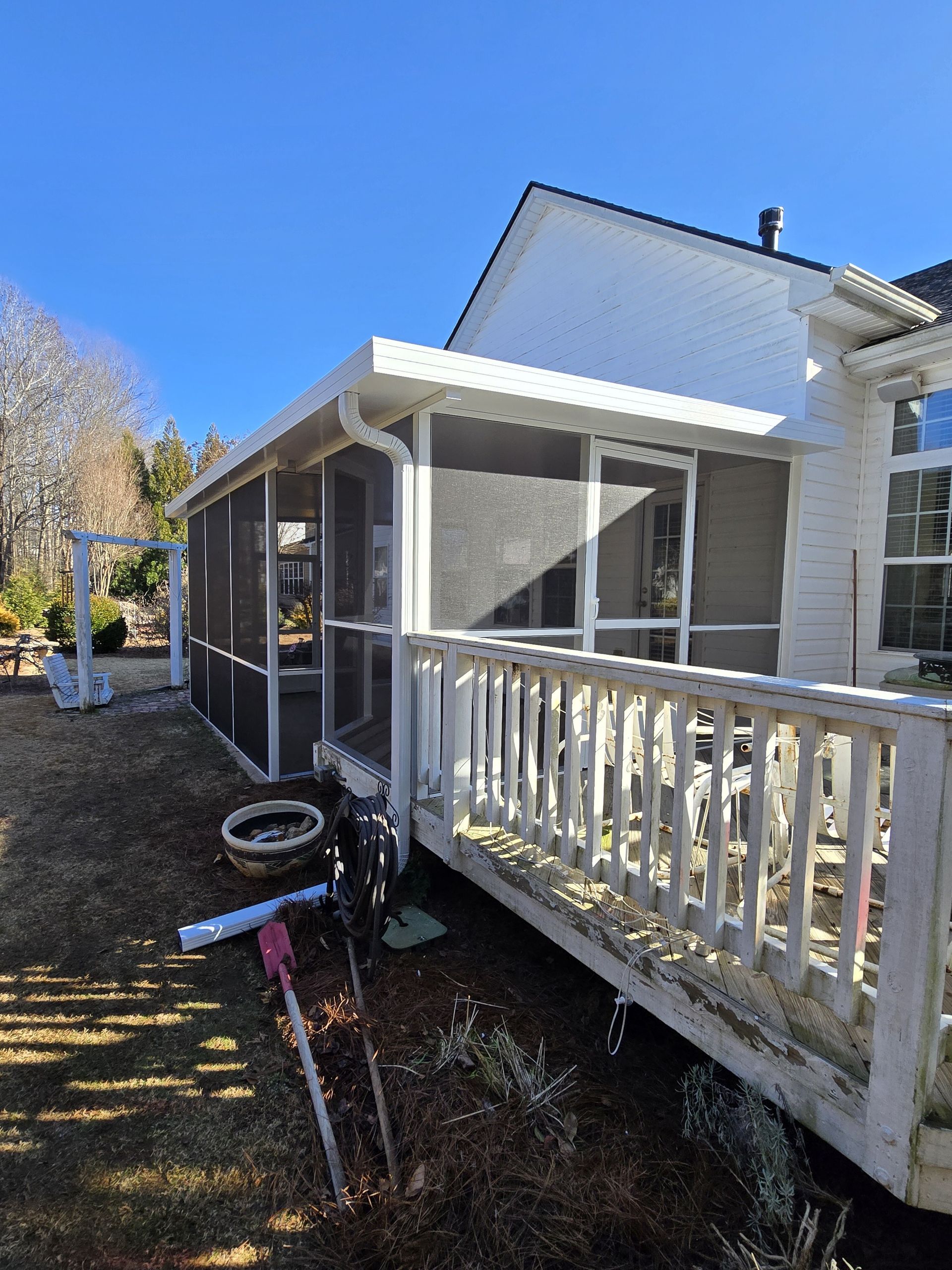 A screened in porch with a white railing and a white house in the background