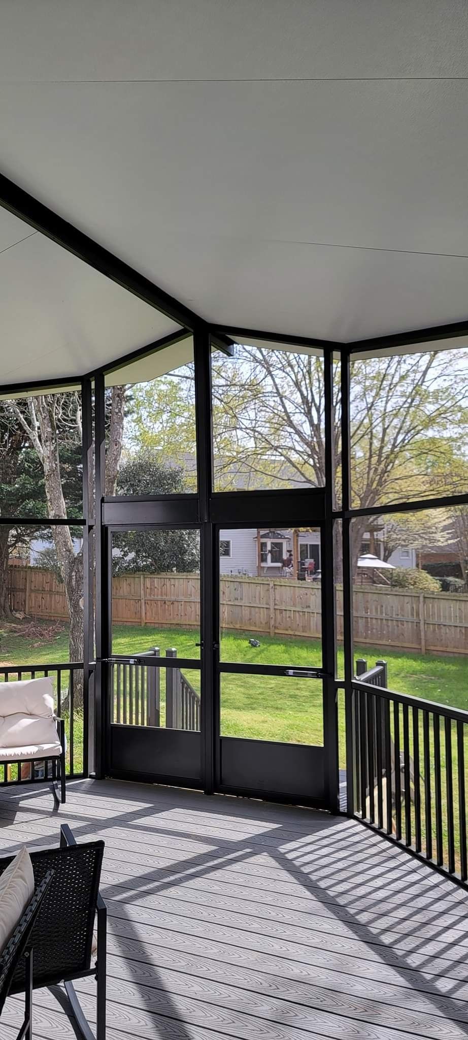A screened in porch with a lot of windows and chairs.
