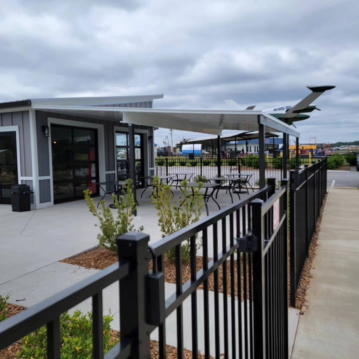 A fence surrounds a building with tables and umbrellas