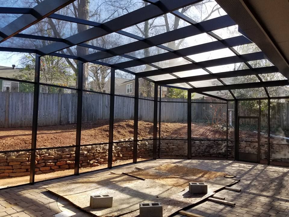 A screened in porch with a glass roof and a fence in the background.