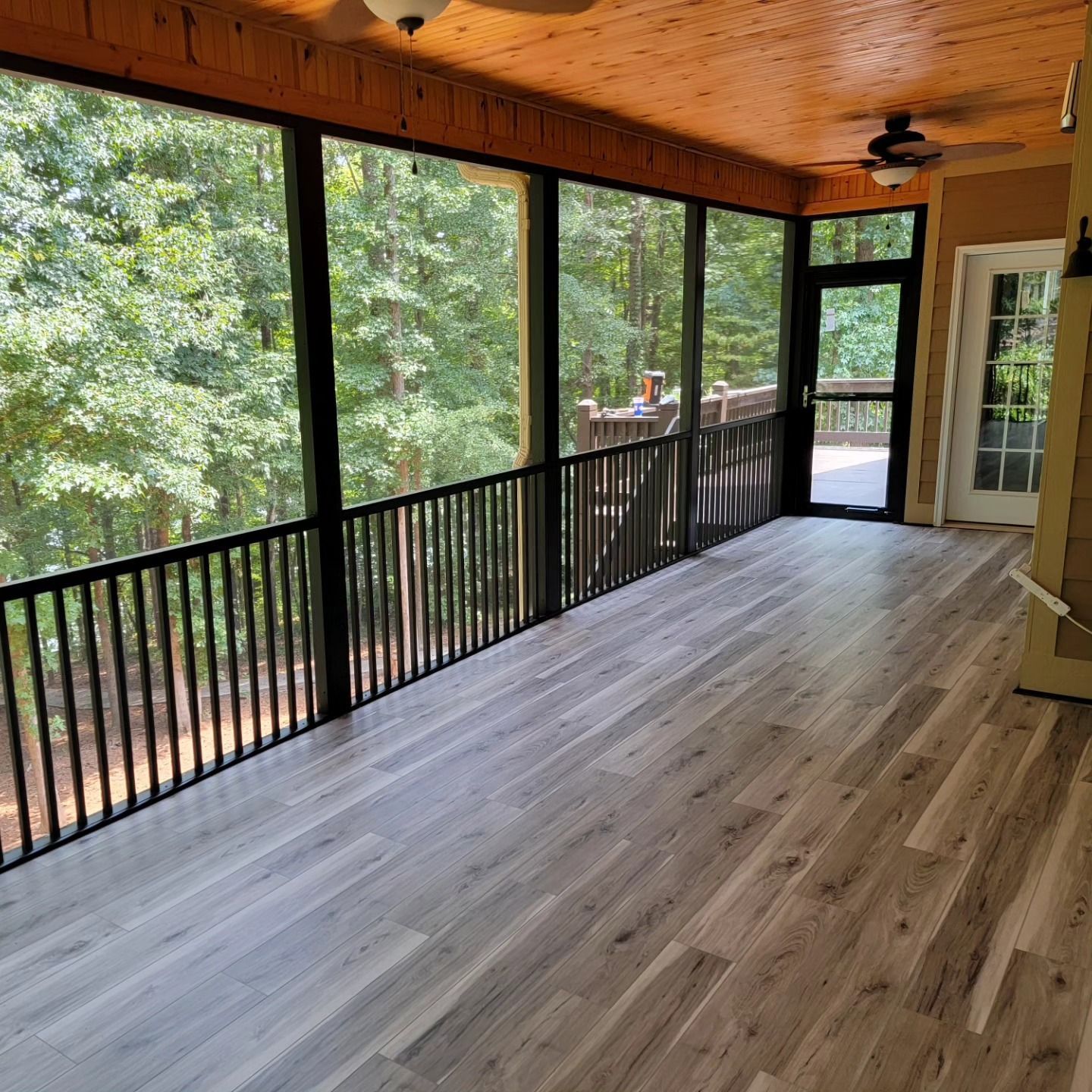 A screened in porch with hardwood floors and a ceiling fan.