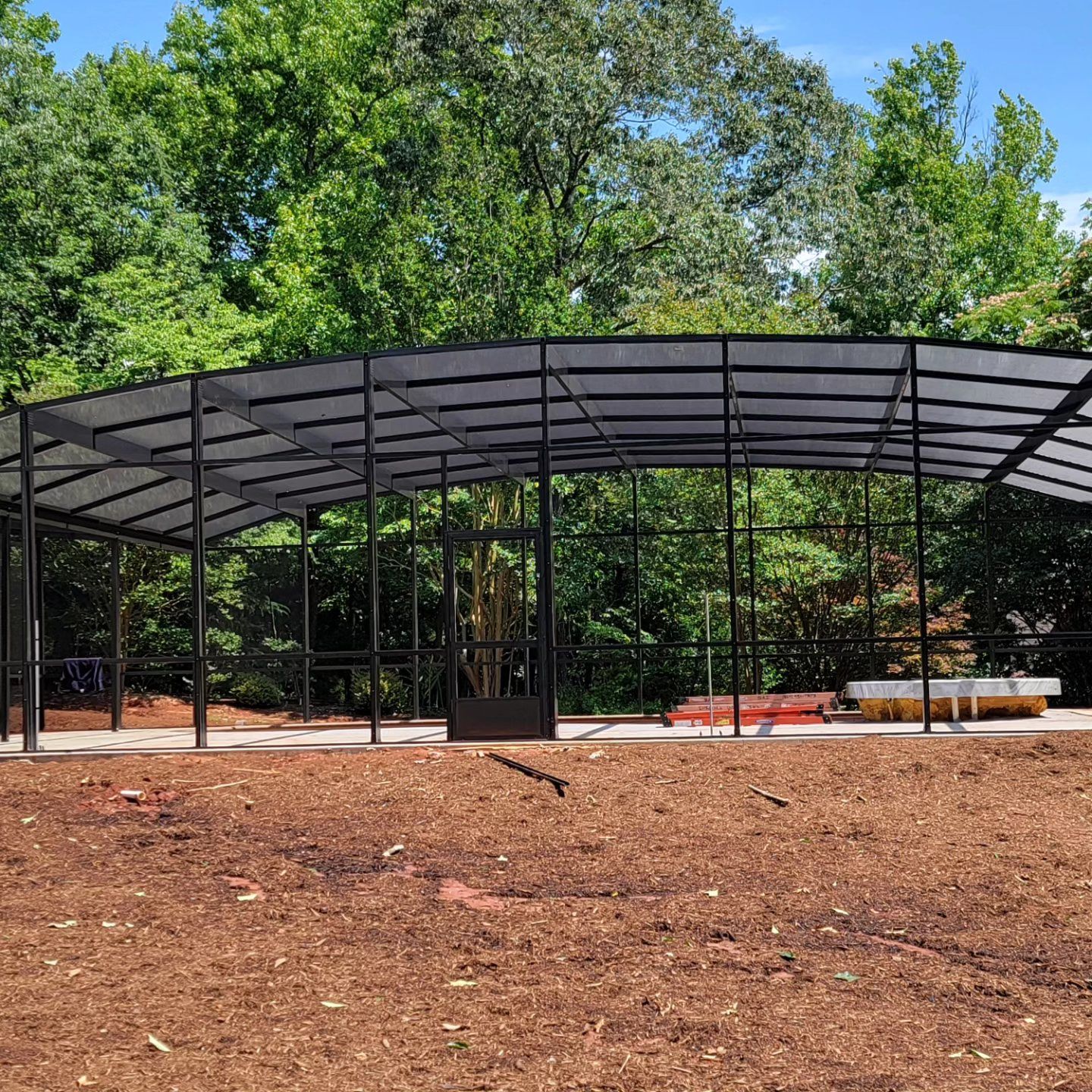 A large metal structure is sitting in the middle of a field surrounded by trees.