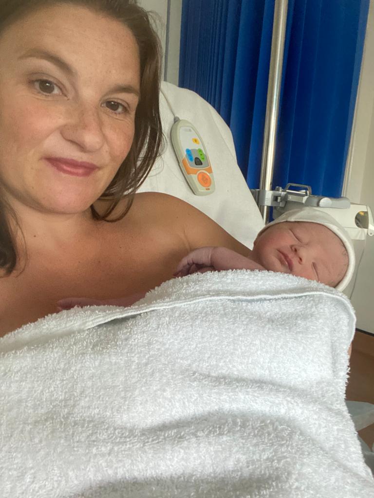 Mother holding newborn in hospital bed, sharing her birth journey on the podcast