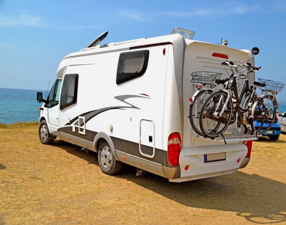 A White RV With Two Bikes Attached to the Back is Parked on the Beach — Waring's Auto Electrical in South Geelong, VIC