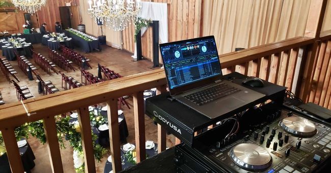 DJ setup overlooking a wedding reception. Laptop on console, ceremony setup below.