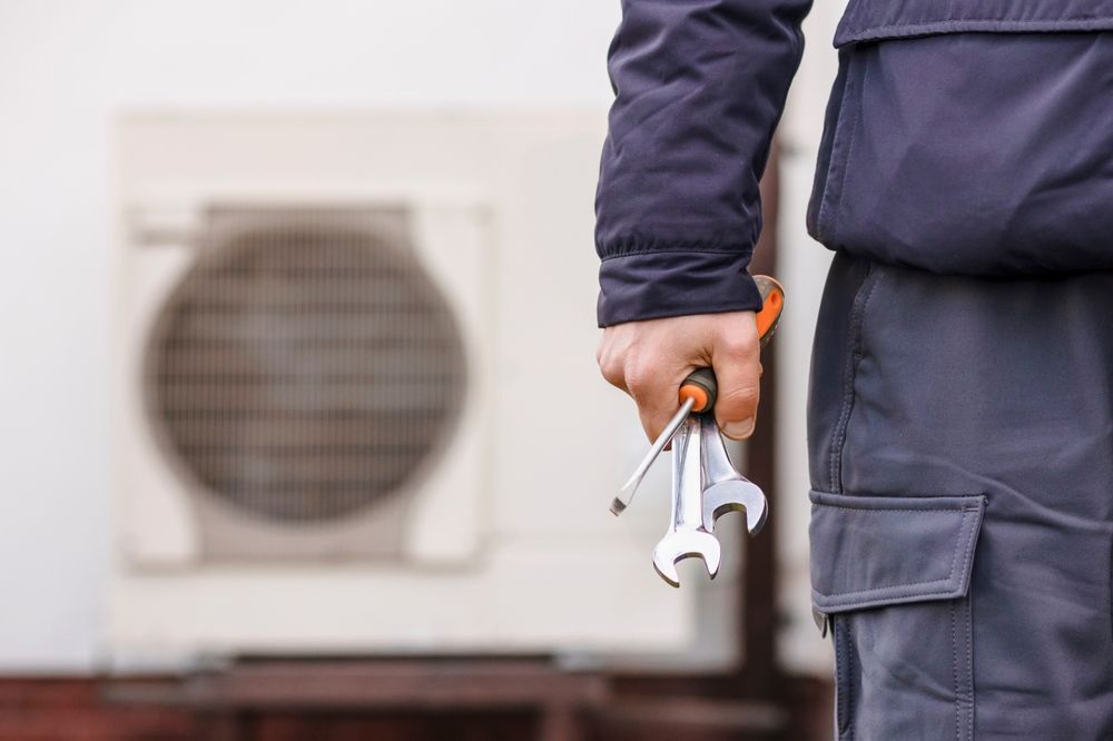A man is holding a pair of wrenches in front of an air conditioner.