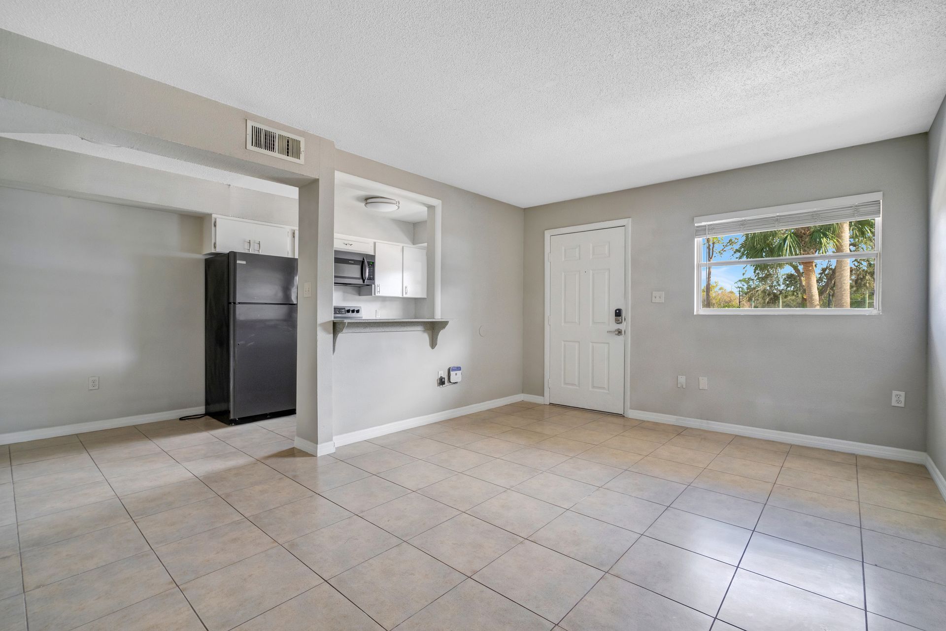 An empty living room with a black refrigerator and a window.
