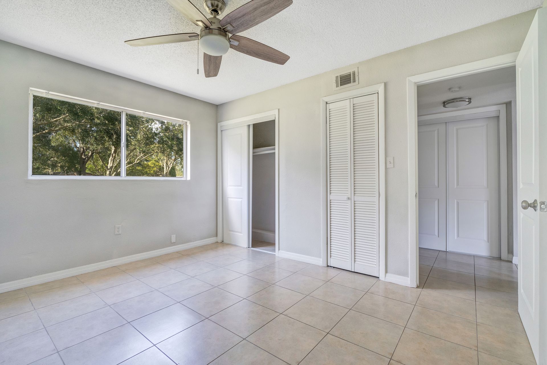 An empty bedroom with a ceiling fan and a window.
