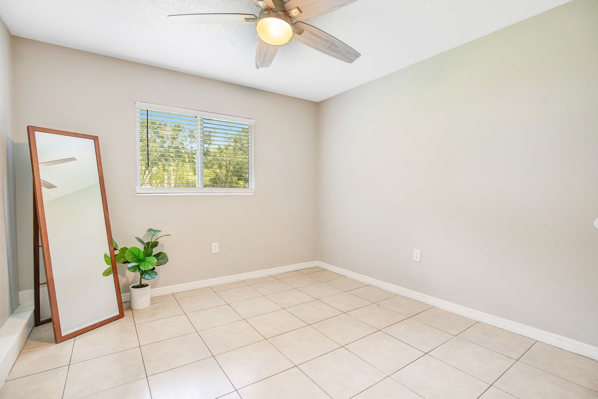 An empty bedroom with a mirror , ceiling fan , and window.