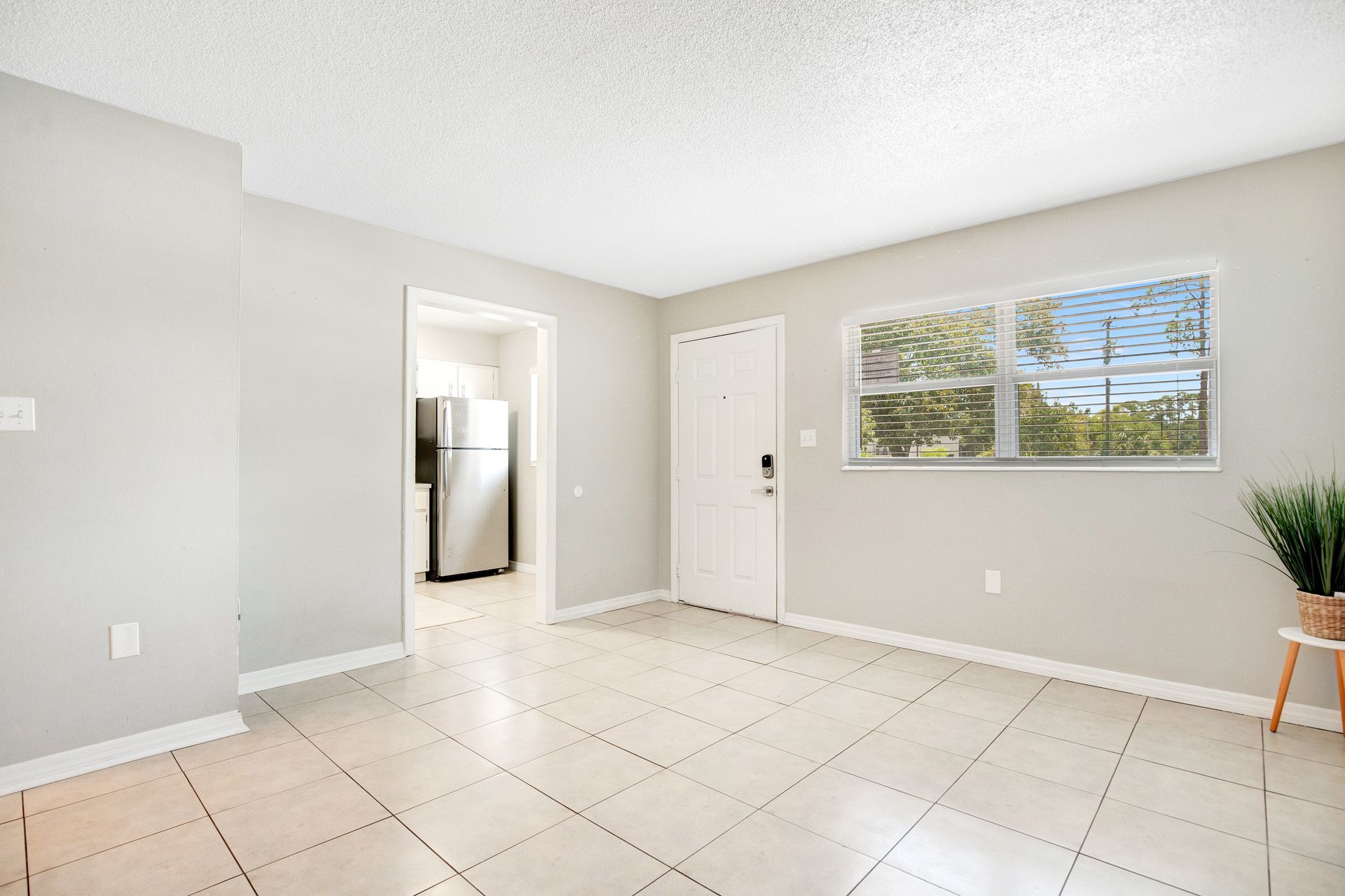 An empty living room with a tiled floor and a refrigerator.