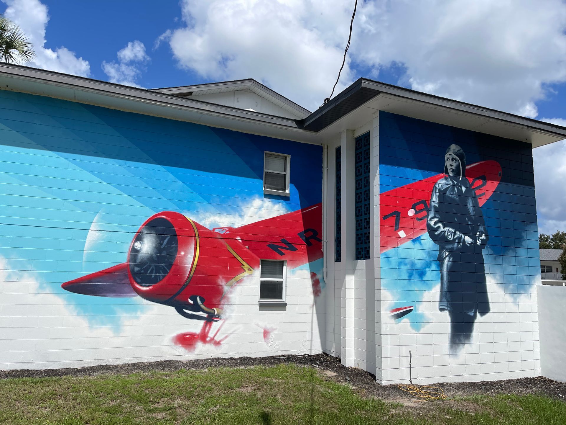 A mural of a man standing next to a red airplane on the side of a building.
