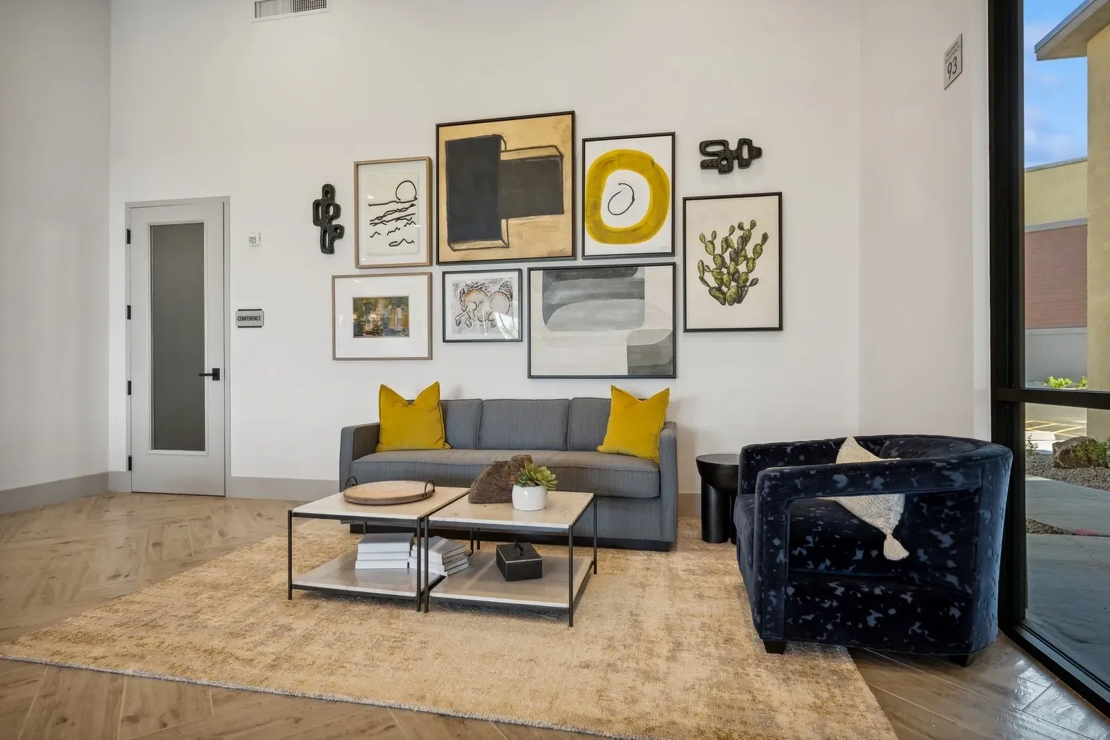 Modern living room with gray sofa, yellow pillows, gallery wall, coffee table, and navy armchair
