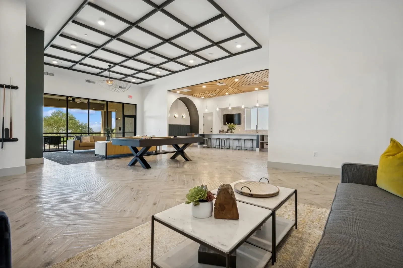Modern open-plan living room with pool table, white kitchen, and large windows overlooking trees