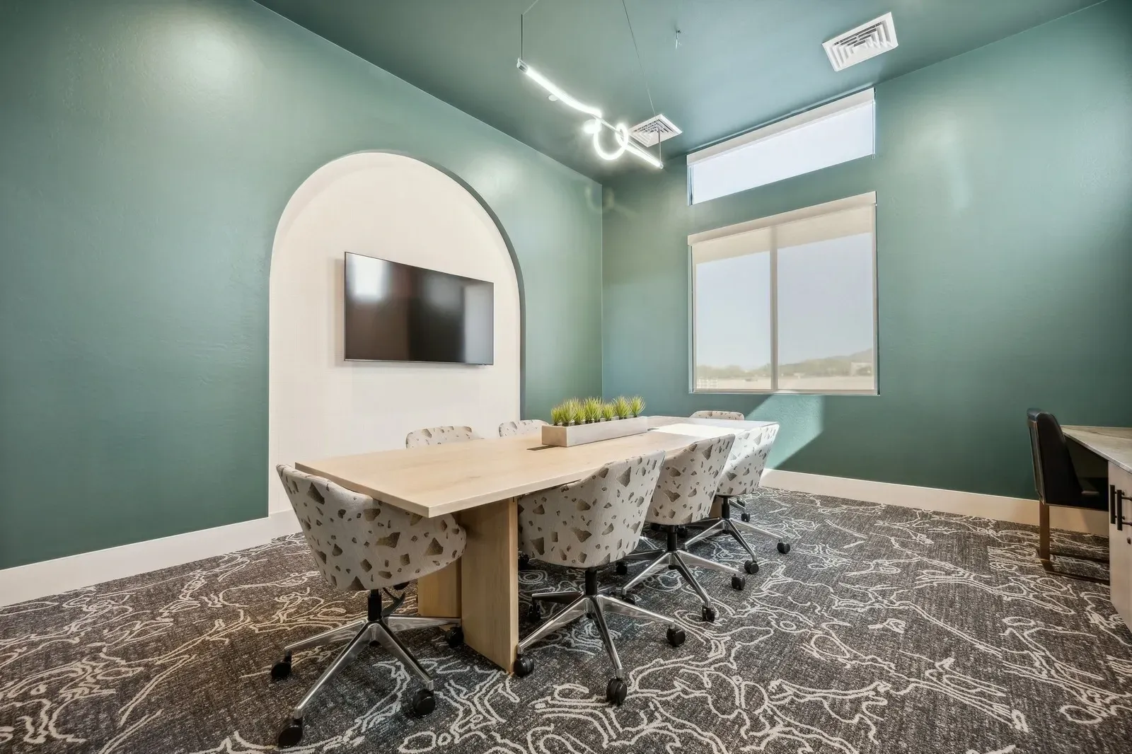 Conference room featuring a large table, comfortable chairs, and a wall-mounted TV, perfect for business meetings or group activities.