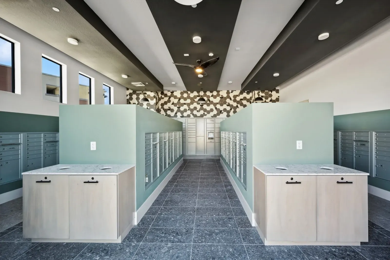Modern mailroom featuring rows of mailboxes and secure package lockers, with stylish countertops and a decorative accent wall.