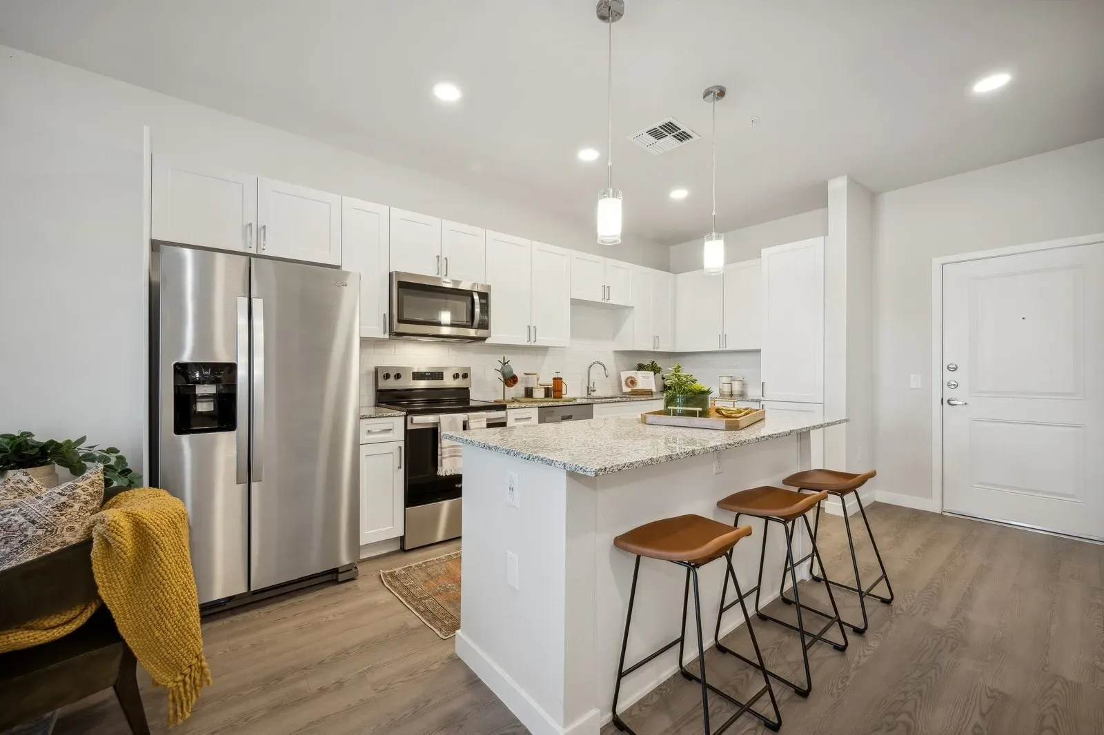 Bright modern kitchen with white cabinets, stainless steel appliances, island, and three stools