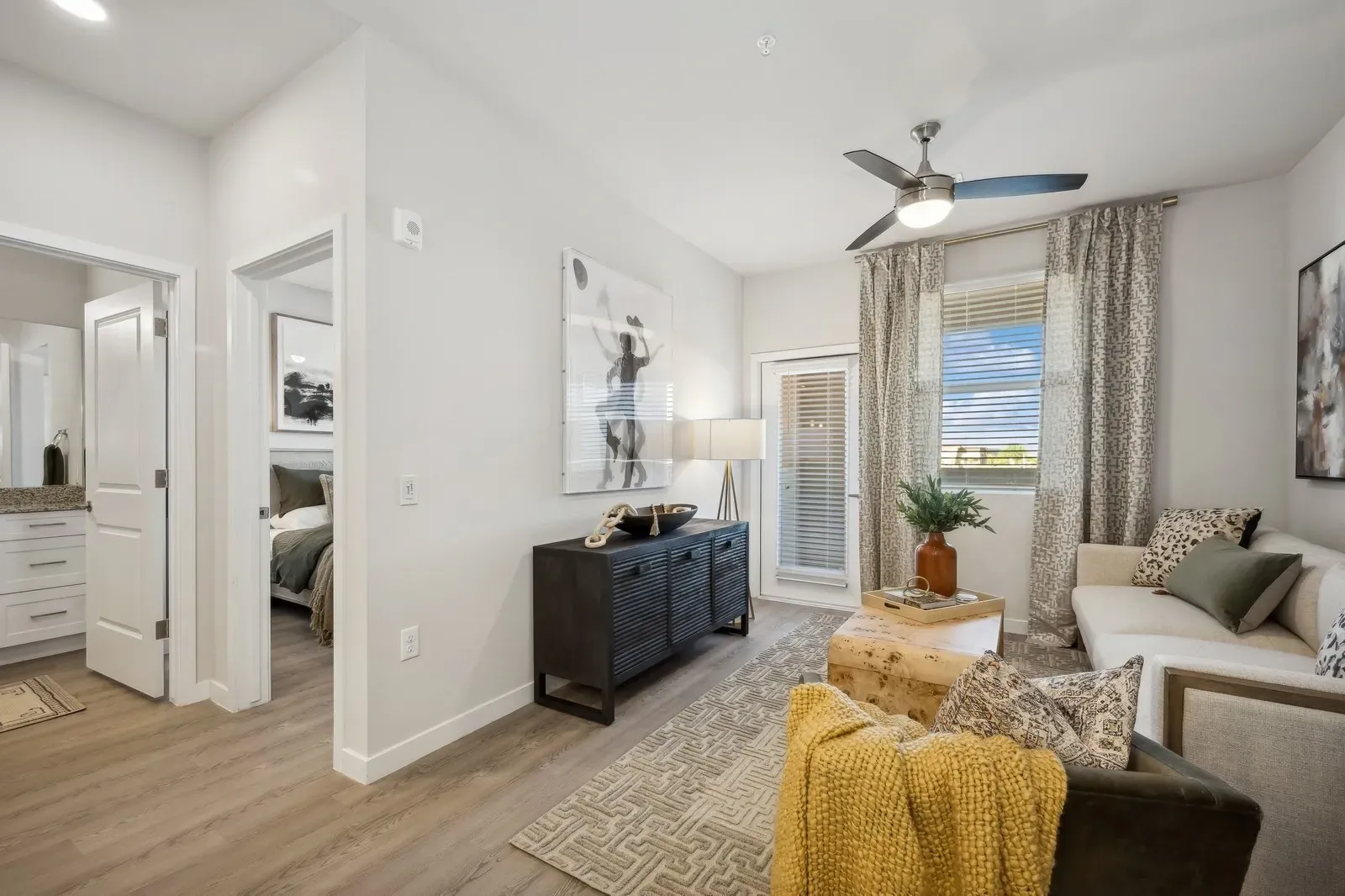 Bright living room with gray sofa, TV console, patterned rug, and balcony doors with curtains