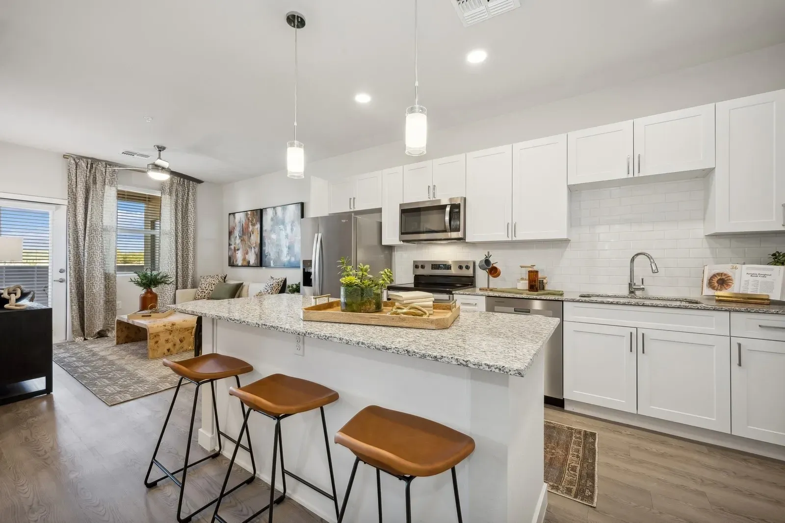 Bright modern kitchen with white cabinets, granite island, and three brown stools