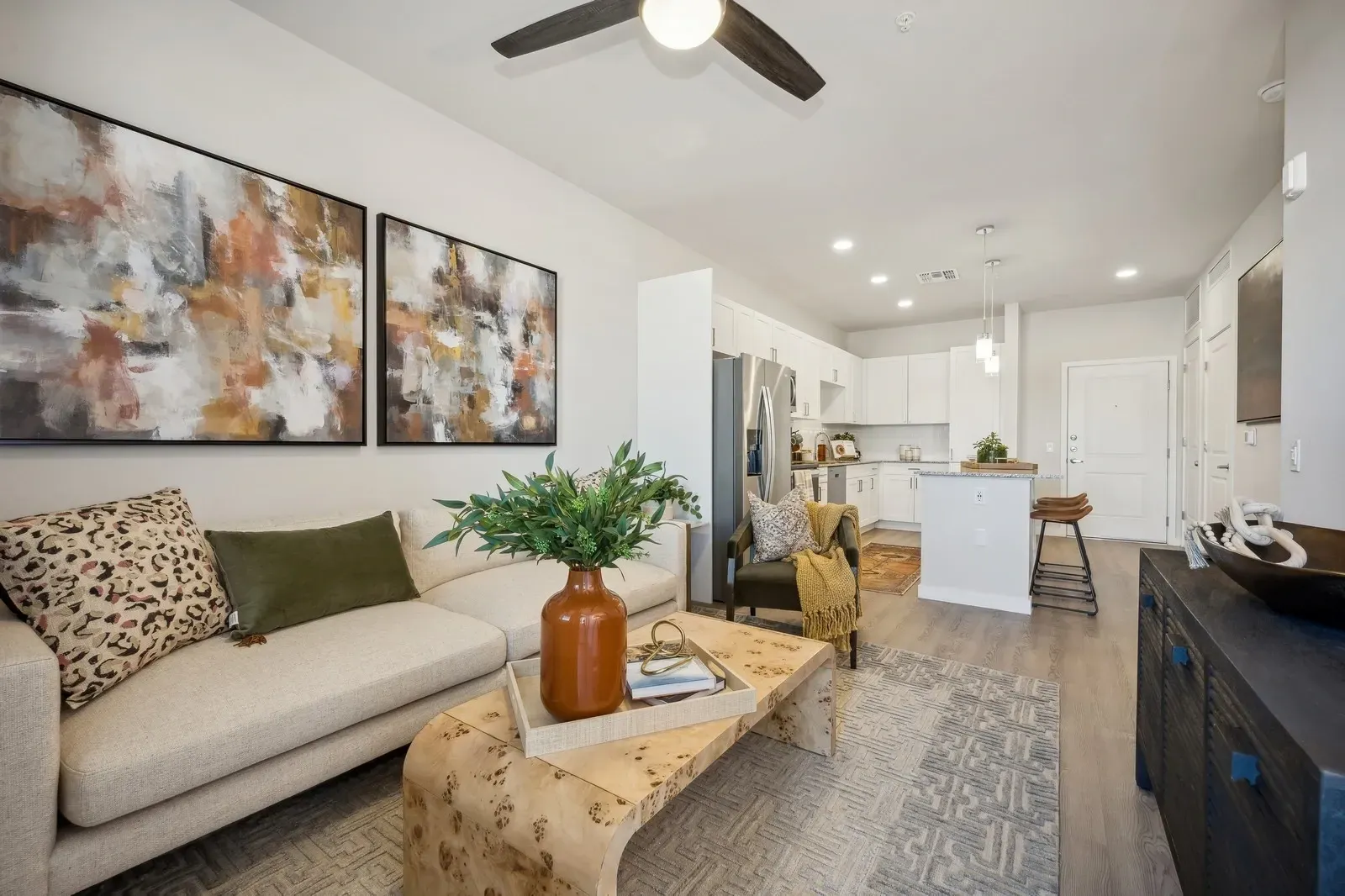 Bright modern open-plan living room with beige sofa, abstract art, wood coffee table, and kitchen island in background