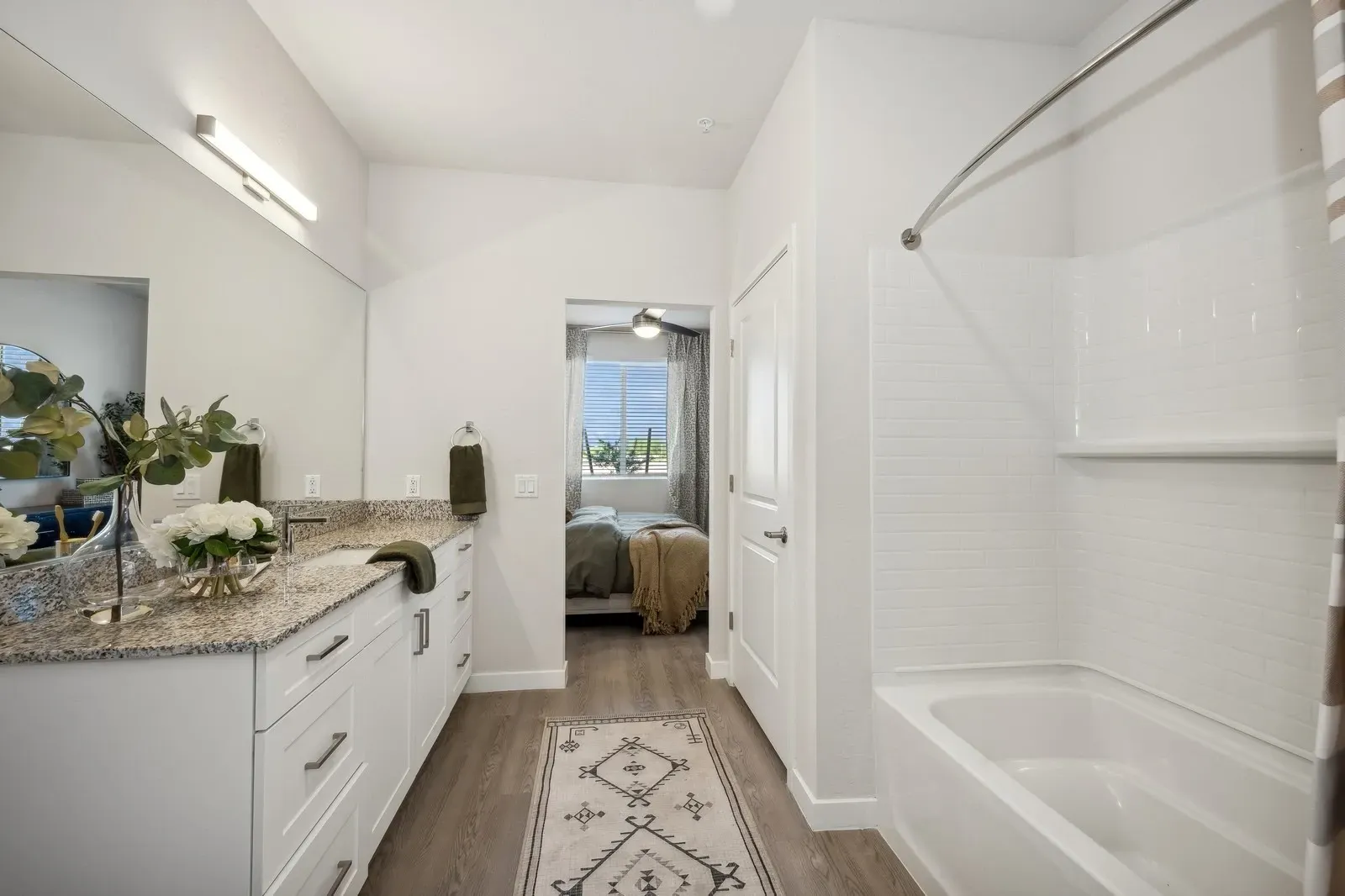 Bright white bathroom with vanity, shower/tub, and doorway to a bedroom or sitting area.